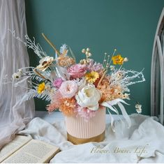 a vase filled with lots of flowers on top of a bed next to an open book