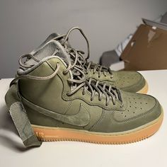 This Is The Big Kids' Version Of The Nike Air Force 1 High Wb, Featuring A Tonal Medium Olive Finish Across The Shoe's Nubuck Upper. Rope Laces And An Adjustable Nylon Ankle Strap Contribute To The Utilitarian Aesthetic That Informs The Design. A Partially Translucent Gum Rubber Sole Unit, Packing An Encapsulated Nike Air Bag, Delivers Both Cushioning And Traction. Nike Air Force 1 Leather Lace-up Shoes, Nike Air Force 1 High-top Leather With Gum Sole, Nike Air Force 1 Streetwear With Round Toe, Casual Nike Air Force 1 Leather Shoes With Laces, Khaki Sneakers With Boost Midsole For Streetwear, Casual Leather Nike Air Force 1, Green Nike Air Force 1 With Gum Sole, Green Leather Nike Air Force 1 With Round Toe, Urban Basketball Shoes With Round Toe For Outdoor