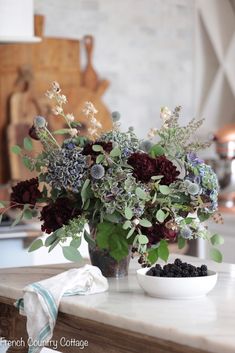 a vase filled with flowers sitting on top of a counter next to a white bowl