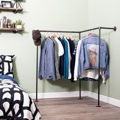 clothes hanging on rail in bedroom next to bed and wall mounted shelf with hat, sweaters and t - shirts