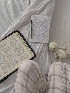 an open book and a stuffed animal are on the bed with a notepad next to it