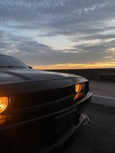 a black car parked on the side of a road at sunset with clouds in the background