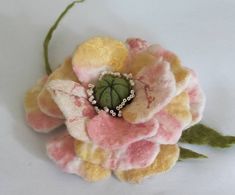 a close up of a flower on a white surface with green leaves and beads in the center