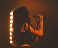 a woman holding a microphone in her right hand and singing into the microphone on stage