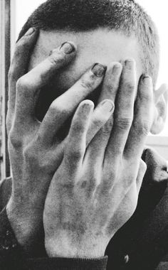 black and white photograph of a man covering his face with both hands while looking out the window