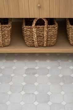 three wicker baskets are sitting on a shelf next to a tiled floor with white hexagonal tiles