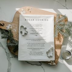 a recipe on a cutting board next to cookie cutters and pine branches with snowflakes