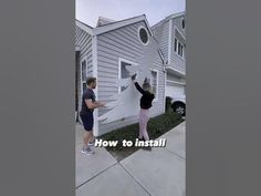 two people are painting the side of a house with white paint and black lettering on it