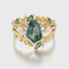 a gold ring with green and white stones on the sides, surrounded by leafy leaves