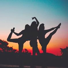 two women are standing in the sunset with their arms around each other and one woman is holding her leg up