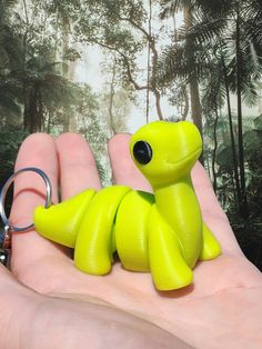 a hand holding a small green toy in it's palm with trees in the background