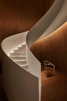 a white spiral staircase next to a chair in a room with wooden walls and flooring