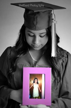 a woman wearing a graduation cap and gown holding a pink frame with a photo in it