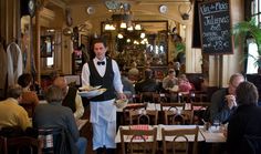 a waiter is holding a plate with food in front of people sitting at tables and eating