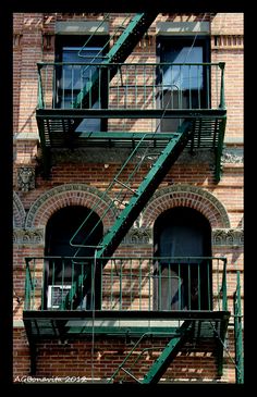 a fire escape on the side of a brick building with green railings and balconies