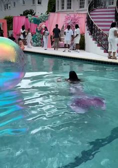 a person in a pool with a ball floating on it's back and people standing around