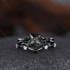 a black diamond engagement ring set on top of a gray stone surface with diamonds in the middle