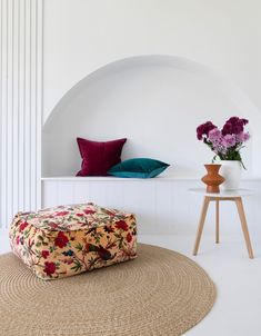 a flowered ottoman sitting on top of a rug next to a vase with flowers