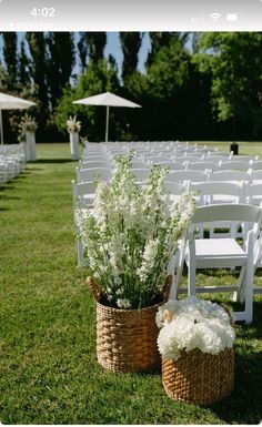 two baskets filled with white flowers sitting on top of a grass covered field next to chairs