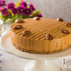 a cake with nuts on top sitting on a table next to purple flowers and plates