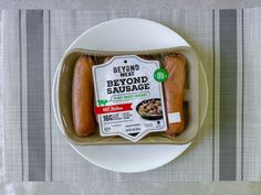 two sausages in a plastic container on a white plate with a striped tablecloth