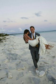 a bride carrying her groom on the beach at sunset in front of an ocean view