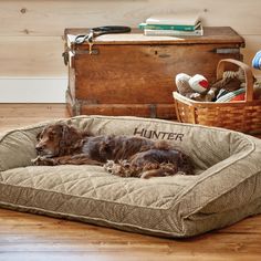 a brown dog laying on top of a bed next to a wooden trunk and basket