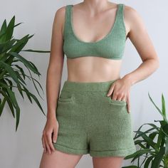 a woman wearing green shorts and a bra top standing in front of a potted plant