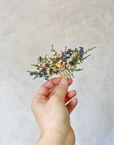 a hand holding a small flower arrangement in it's left hand, against a white background