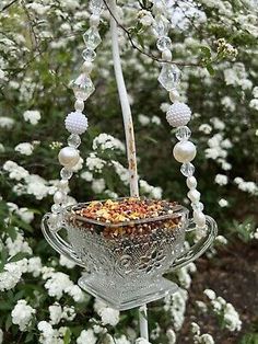 a bird feeder with beads hanging from it's side in front of some flowers