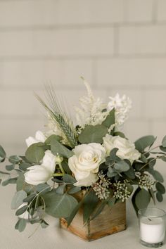 a vase filled with white flowers and greenery on top of a wooden block next to a candle