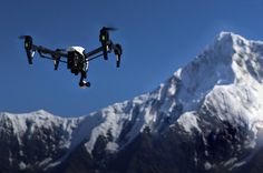 a large black and white remote controlled flying in front of snow covered mountain peaks with green lights