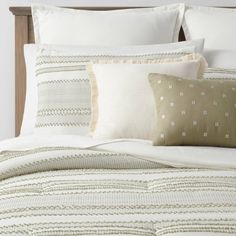 a bed with white and green pillows on top of it next to a wooden headboard