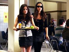 two women standing in front of a table with food on it and one holding a tray