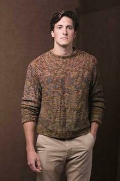 a man standing in front of a brown wall wearing a sweater and khaki pants