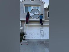 two people on a ladder painting the outside of a house with a clock in it