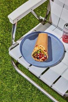 a plate with a burrito on it sitting in a lawn chair next to a drink