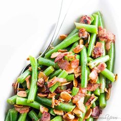 a white bowl filled with green beans, bacon and toasted almonds next to a fork