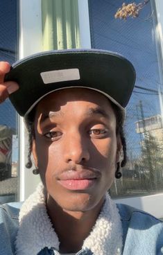 a young man wearing a hat and posing for the camera in front of a building