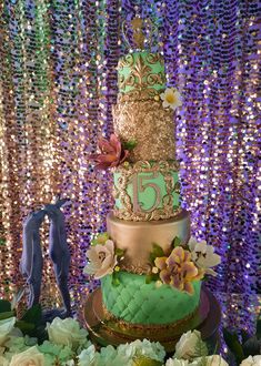 a three tiered cake sitting on top of a table covered in flowers and sequins