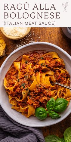 a white bowl filled with pasta and meat sauce on top of a wooden table next to bread