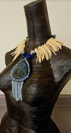 A labrodorite or spectrolite sculpted pendant with sapphire blue and silver aurora borealis rhinestone fringe is the focal point on this one-of-a-kind statement necklace or chest piece. Flanking the pendant are two sapphire blue crystals, silver aurora borealis rhinestone rondelles and stamped silver tone tribal bicones. The remainder of the necklace is blonde coconut fringe with black lava beads, silver tone metal bi-cones and blue crystals finishing the back. This lightweight and comfortable p Unique Handmade Sapphire Necklace, Handmade Bohemian Kyanite Jewelry, Artisan Blue Labradorite Necklace, Artisan Sapphire Jewelry, Bohemian Jewelry With Gemstone Accents And Labradorite, Unique Lapis Lazuli Pendant Jewelry, Artisan Labradorite Necklaces With Stones, Artisan Labradorite Gemstone Bead Jewelry, Unique Labradorite Stone Necklaces