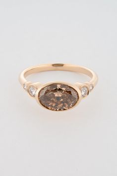 an oval shaped brown diamond ring with three diamonds on the band and side stones in yellow gold