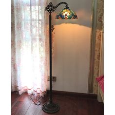 a floor lamp with a stained glass shade on it in front of a curtained window