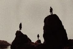 two people standing on top of rocks near the ocean