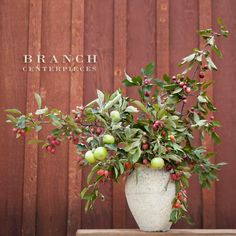 a white vase filled with lots of green and red berries on top of a wooden table