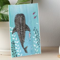 a painting of a whale swimming in the ocean with fish and plants around it art board print