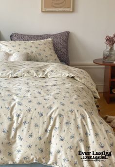 a bed with white sheets and blue flowers on it in a room next to a table