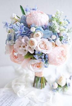 a bouquet of pink and blue flowers on a white table with a book in the background