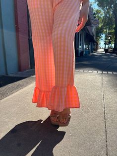 These fun and quirky pants will add some excitement to your wardrobe. The wide leg, elastic waistband, and relaxed fit offer comfort and versatility, while the pink and orange gingham and ruffled hemline add a playful touch. Perfect for dressing up or down, these pants are a dream come true! Casual Cotton Bottoms With Flared Hem, Trendy Wide Leg Gingham Pants, Casual Gingham Wide Leg Bottoms, Casual Bottoms With Flared Hem For Spring, Casual Wide Leg Gingham Bottoms, Spring Vacation Gingham Bottoms, Spring Flare Wide Leg Pants With Elastic Waistband, Trendy Flared Hem Summer Pants, Casual Pink Wide Leg Flare Pants